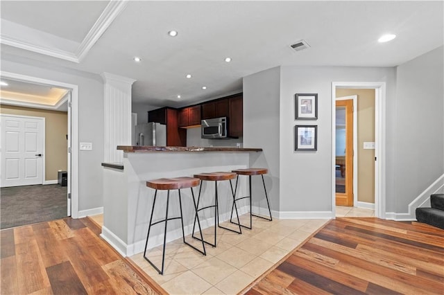 kitchen with visible vents, appliances with stainless steel finishes, a kitchen breakfast bar, ornamental molding, and recessed lighting