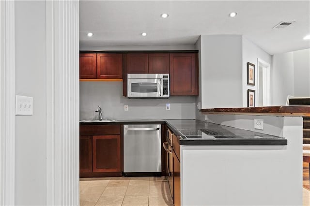 kitchen featuring a peninsula, a sink, visible vents, appliances with stainless steel finishes, and dark countertops