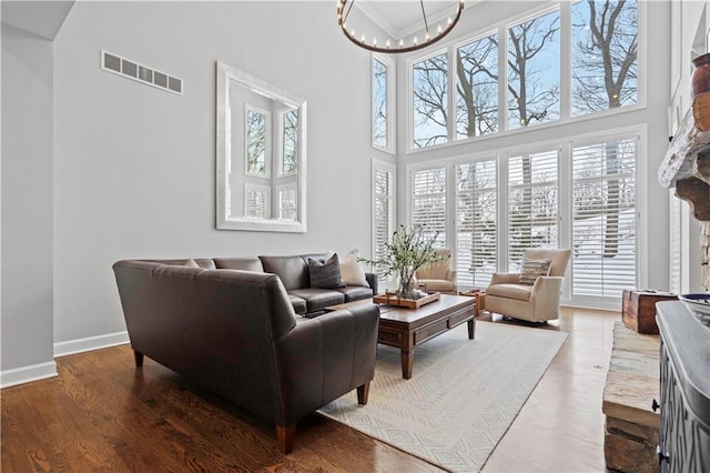 living area featuring baseboards, visible vents, a towering ceiling, wood finished floors, and a chandelier