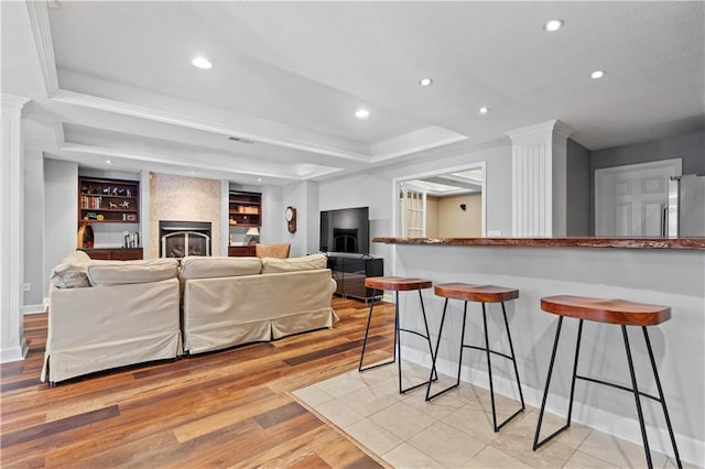 living area with light wood-type flooring, a tray ceiling, a fireplace, and recessed lighting