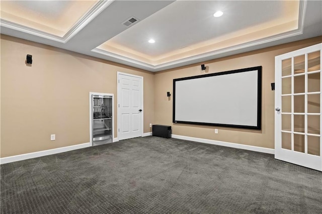 home theater room with visible vents, a tray ceiling, dark colored carpet, and baseboards