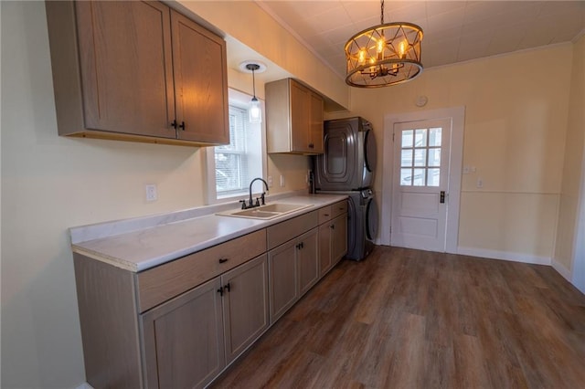 kitchen with dark hardwood / wood-style floors, pendant lighting, stacked washer / dryer, sink, and an inviting chandelier