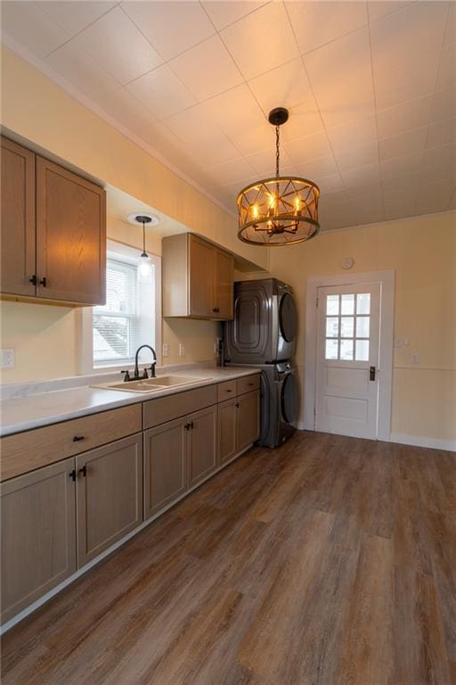 kitchen featuring stacked washer / drying machine, sink, dark hardwood / wood-style flooring, and decorative light fixtures