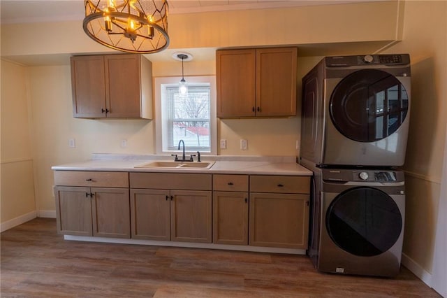 laundry area featuring cabinets, stacked washer and clothes dryer, sink, and light hardwood / wood-style flooring