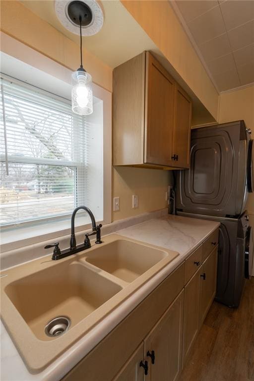 kitchen with dark wood-type flooring, stacked washer and clothes dryer, sink, crown molding, and hanging light fixtures