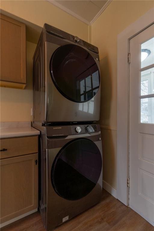 washroom with stacked washer / dryer, ornamental molding, cabinets, and light hardwood / wood-style flooring