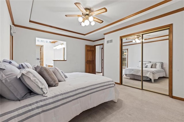 bedroom featuring light colored carpet, ceiling fan, a tray ceiling, crown molding, and a closet