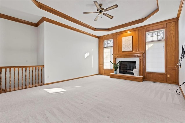 unfurnished living room featuring a raised ceiling, ornamental molding, light colored carpet, and ceiling fan