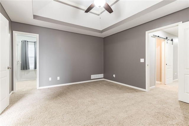 carpeted empty room featuring ceiling fan, a barn door, and a raised ceiling