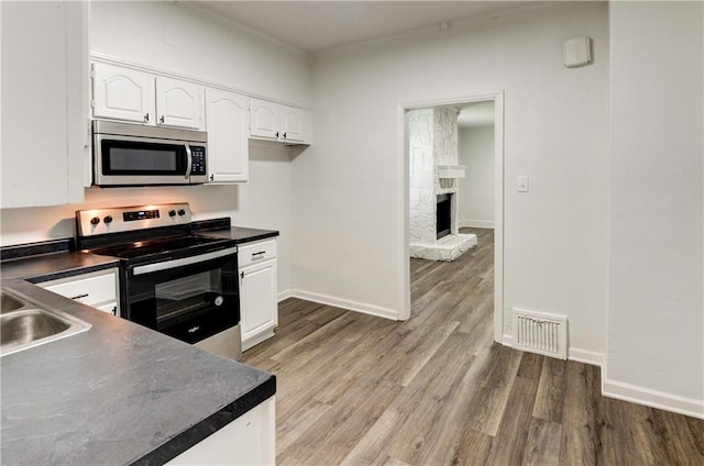 kitchen with white cabinets, stainless steel appliances, a fireplace, sink, and light hardwood / wood-style flooring