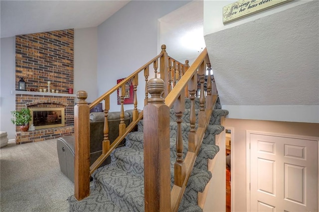 staircase with lofted ceiling, carpet, a brick fireplace, and a textured ceiling