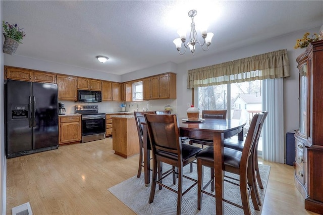 kitchen featuring an inviting chandelier, decorative light fixtures, light wood-type flooring, and black appliances