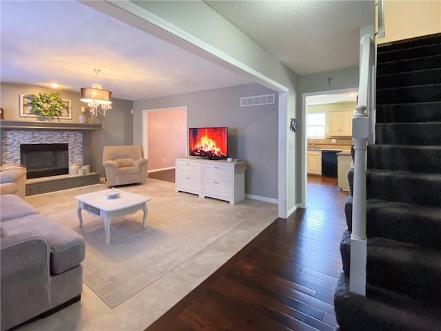 living room featuring hardwood / wood-style flooring, a stone fireplace, and an inviting chandelier