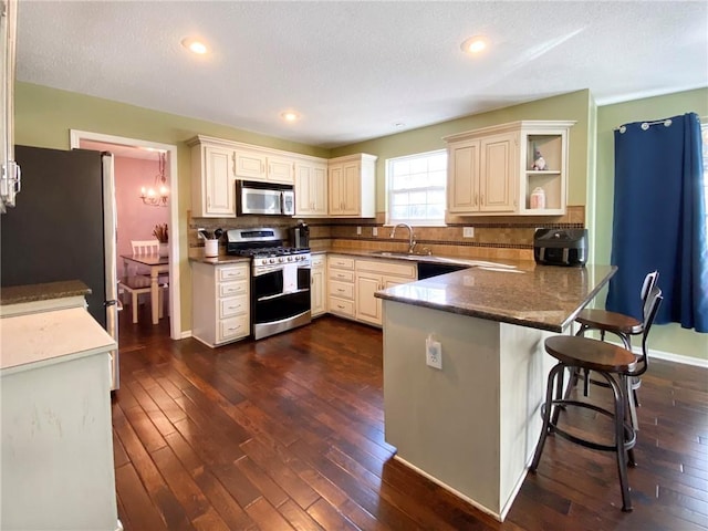 kitchen featuring appliances with stainless steel finishes, sink, dark hardwood / wood-style flooring, a kitchen breakfast bar, and kitchen peninsula