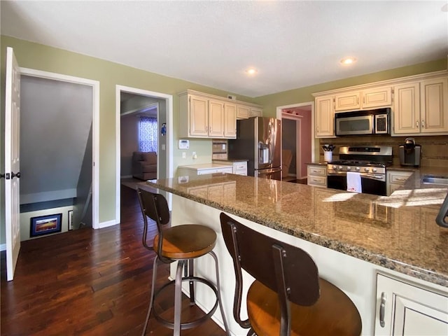 kitchen with dark wood-type flooring, a breakfast bar, dark stone counters, stainless steel appliances, and backsplash