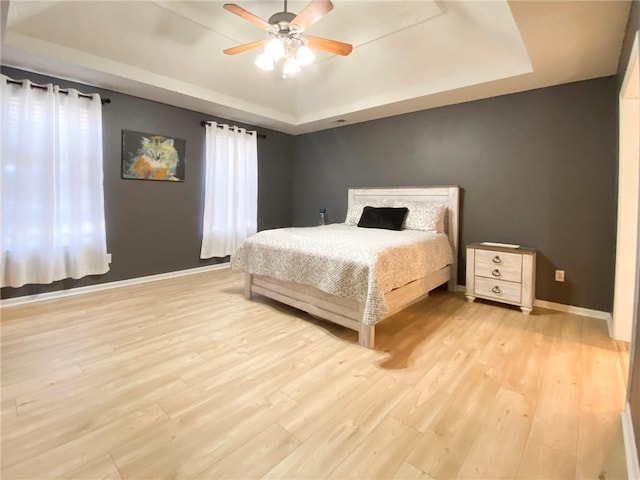 bedroom with a raised ceiling, ceiling fan, and light hardwood / wood-style floors