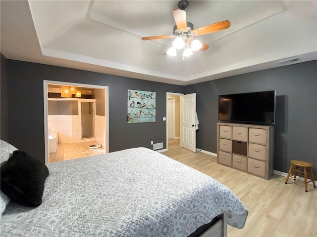 bedroom featuring ceiling fan, connected bathroom, light wood-type flooring, and a tray ceiling