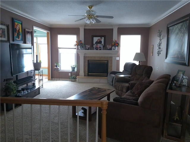 living room with ceiling fan, a tiled fireplace, a textured ceiling, carpet floors, and ornamental molding