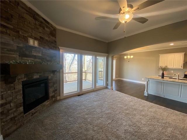 unfurnished living room with a fireplace, crown molding, dark carpet, baseboards, and ceiling fan with notable chandelier