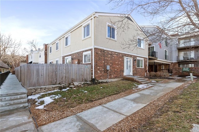 view of front facade with stucco siding, fence, and brick siding