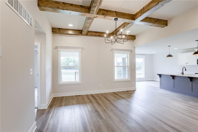 unfurnished dining area featuring sink, a healthy amount of sunlight, light hardwood / wood-style flooring, and beamed ceiling