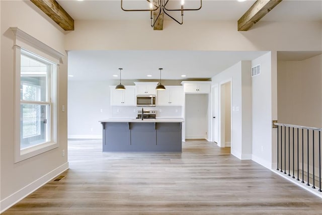 kitchen featuring hanging light fixtures, appliances with stainless steel finishes, white cabinets, a center island with sink, and beamed ceiling