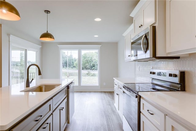 kitchen with appliances with stainless steel finishes, tasteful backsplash, white cabinetry, sink, and decorative light fixtures