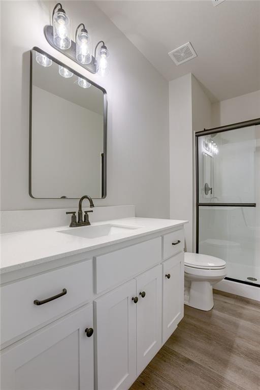 bathroom featuring wood-type flooring, toilet, a shower with door, and vanity