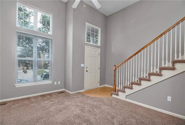 entryway featuring light carpet, a high ceiling, a ceiling fan, baseboards, and stairway