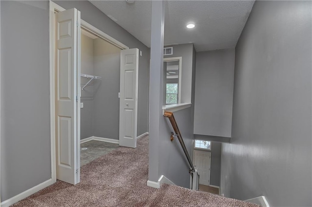 hallway featuring baseboards, visible vents, light colored carpet, and an upstairs landing