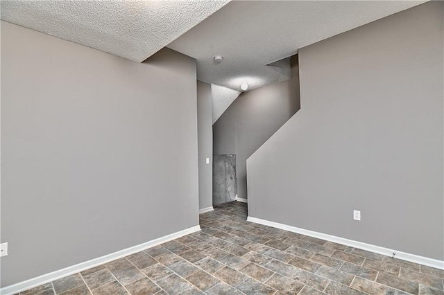 interior space featuring a textured ceiling, stone finish flooring, and baseboards