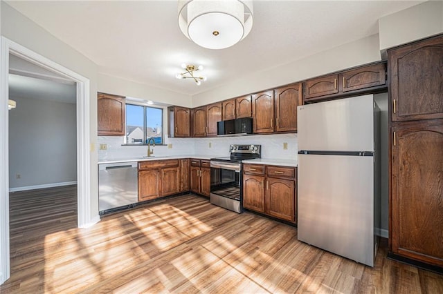 kitchen featuring light hardwood / wood-style floors, sink, dark brown cabinetry, backsplash, and stainless steel appliances