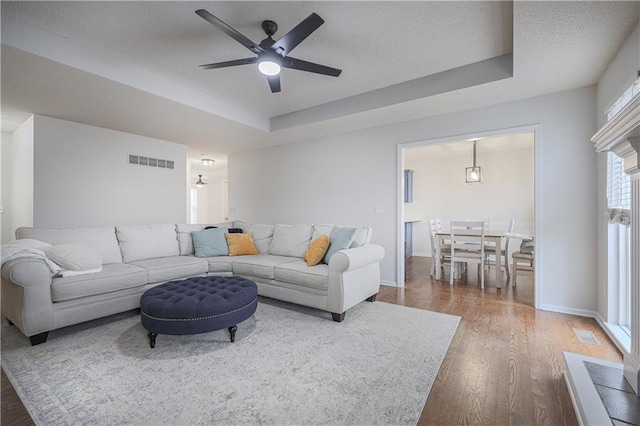 living room with a raised ceiling, ceiling fan, wood-type flooring, and a textured ceiling