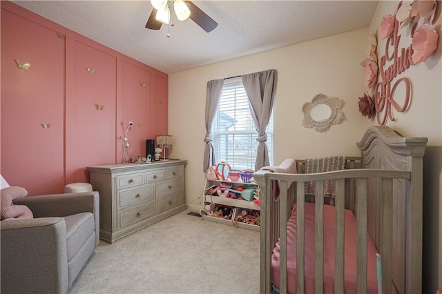 carpeted bedroom featuring a crib, a textured ceiling, and ceiling fan