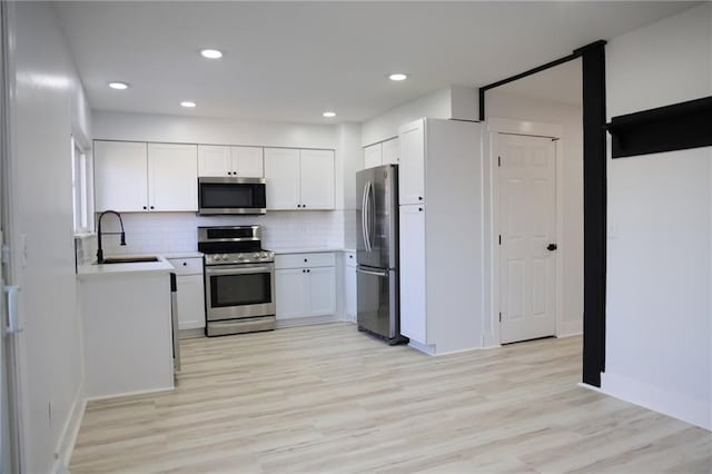 kitchen featuring sink, white cabinetry, tasteful backsplash, light wood-type flooring, and stainless steel appliances