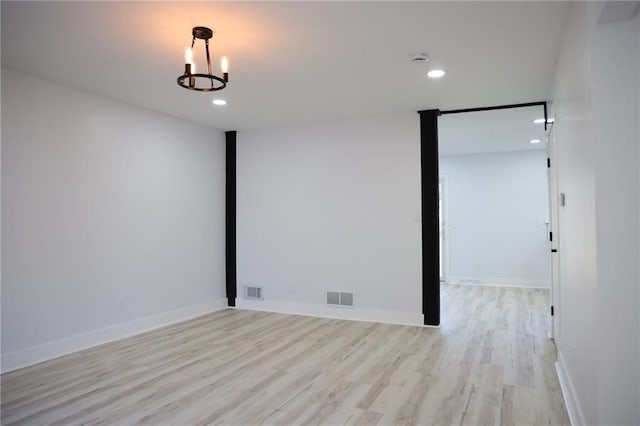 empty room featuring a chandelier and light wood-type flooring