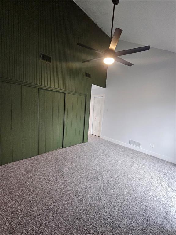 unfurnished bedroom with wooden walls, high vaulted ceiling, ceiling fan, and carpet flooring