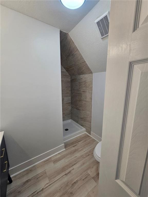 bathroom featuring lofted ceiling, hardwood / wood-style floors, vanity, a shower, and toilet