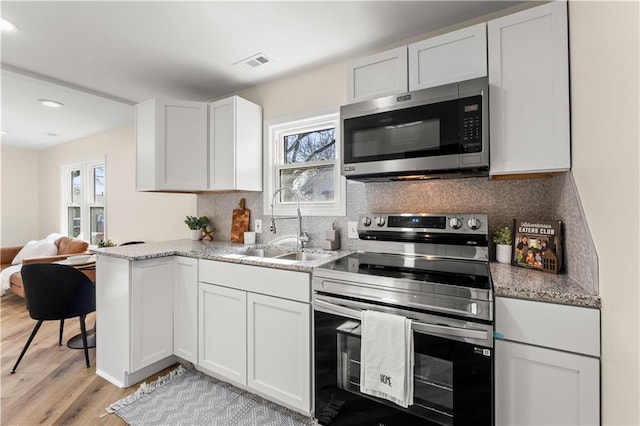 kitchen with appliances with stainless steel finishes, white cabinetry, sink, decorative backsplash, and light wood-type flooring