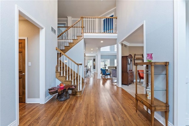 entrance foyer featuring ornamental molding, wood-type flooring, and a towering ceiling