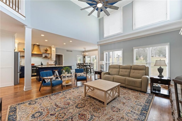 living room featuring ornate columns, ceiling fan with notable chandelier, and dark hardwood / wood-style flooring