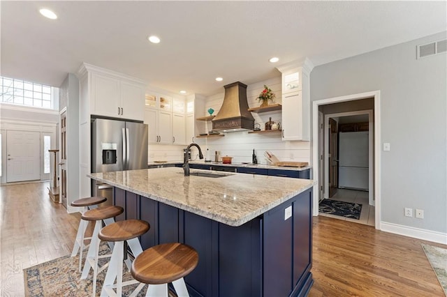 kitchen with white cabinetry, fridge, sink, and custom range hood