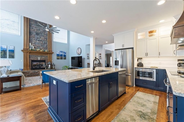 kitchen with sink, blue cabinetry, a kitchen island with sink, stainless steel appliances, and white cabinets