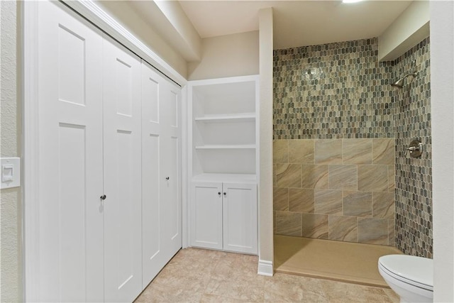 bathroom featuring tile patterned flooring, built in shelves, tiled shower, and toilet