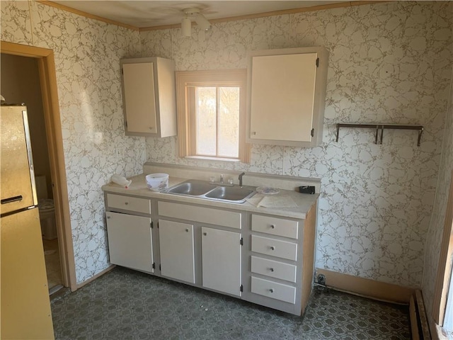 kitchen with sink, white cabinets, ornamental molding, and refrigerator