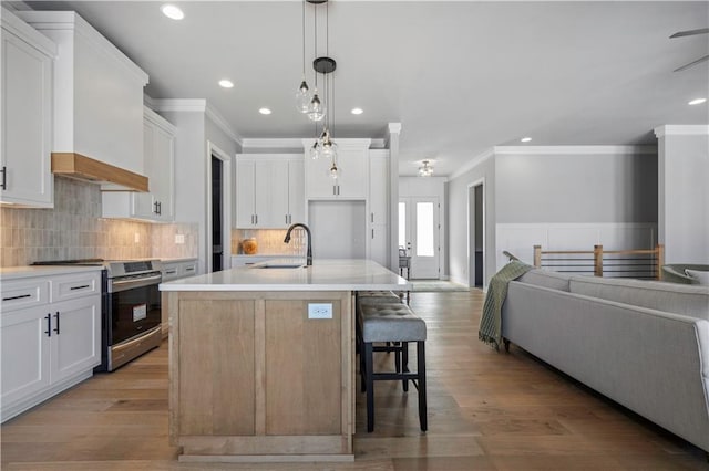 kitchen featuring white cabinets, a kitchen island with sink, hanging light fixtures, and stainless steel range with electric cooktop