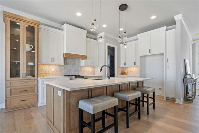 kitchen with a kitchen island with sink, white cabinets, decorative light fixtures, sink, and light hardwood / wood-style flooring