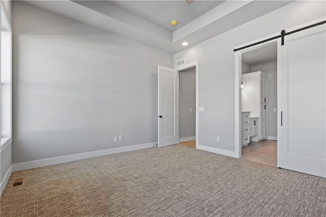 unfurnished bedroom featuring multiple windows, ensuite bathroom, a raised ceiling, and a barn door