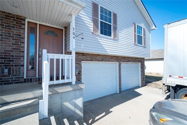 doorway to property with an attached garage, concrete driveway, and brick siding