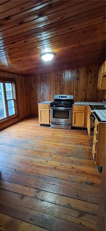 kitchen featuring dark wood-type flooring, wooden ceiling, wooden walls, gas stove, and tile counters